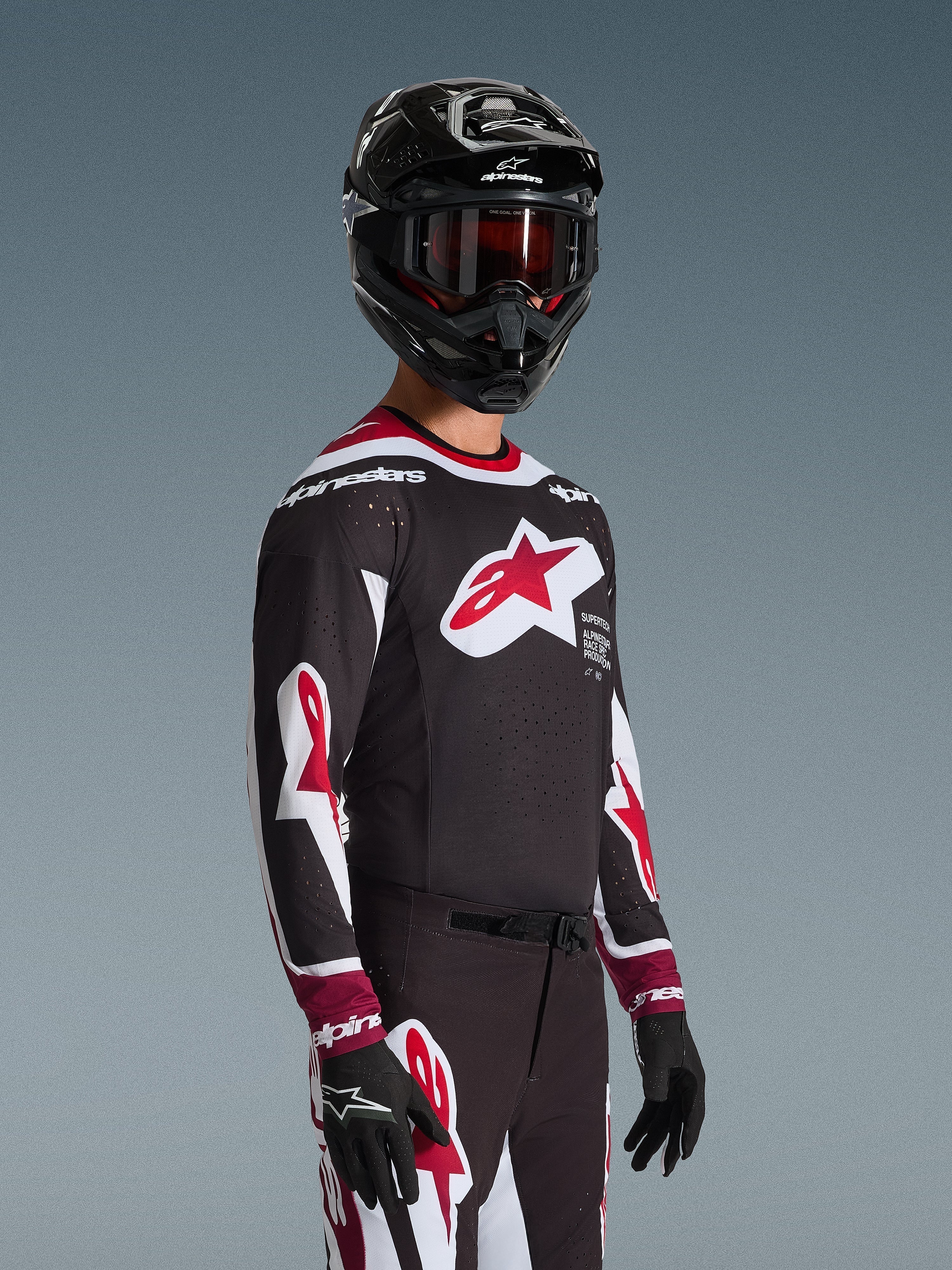 Alpinestars 2026 Supertech AFD Vista Jersey, pilota di motocross con abbigliamento da gara completo, maglia nera con accenti rossi e bianchi, grande logo sul petto, traforature laser, indossata con pantaloni coordinati, casco nero e maschera rossa, completo coordinato per gare fuoristrada