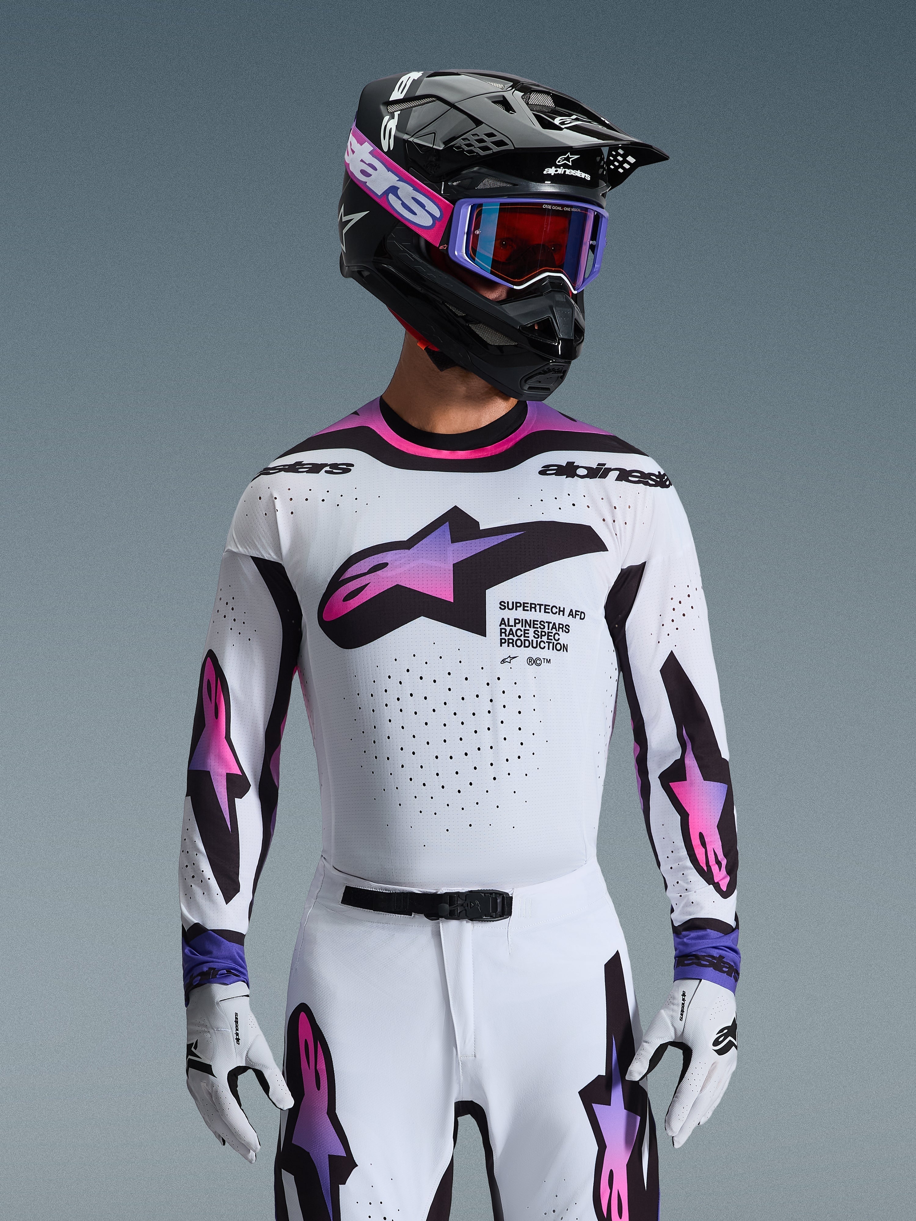Pilota di motocross che indossa la maglia Supertech AFD Vista 2026 in bianco, viola e nero, con casco nero e logo rosa, occhiali viola e guanti bianchi coordinati, abbigliamento con vestibilità atletica progettato per prestazioni professionali off-road