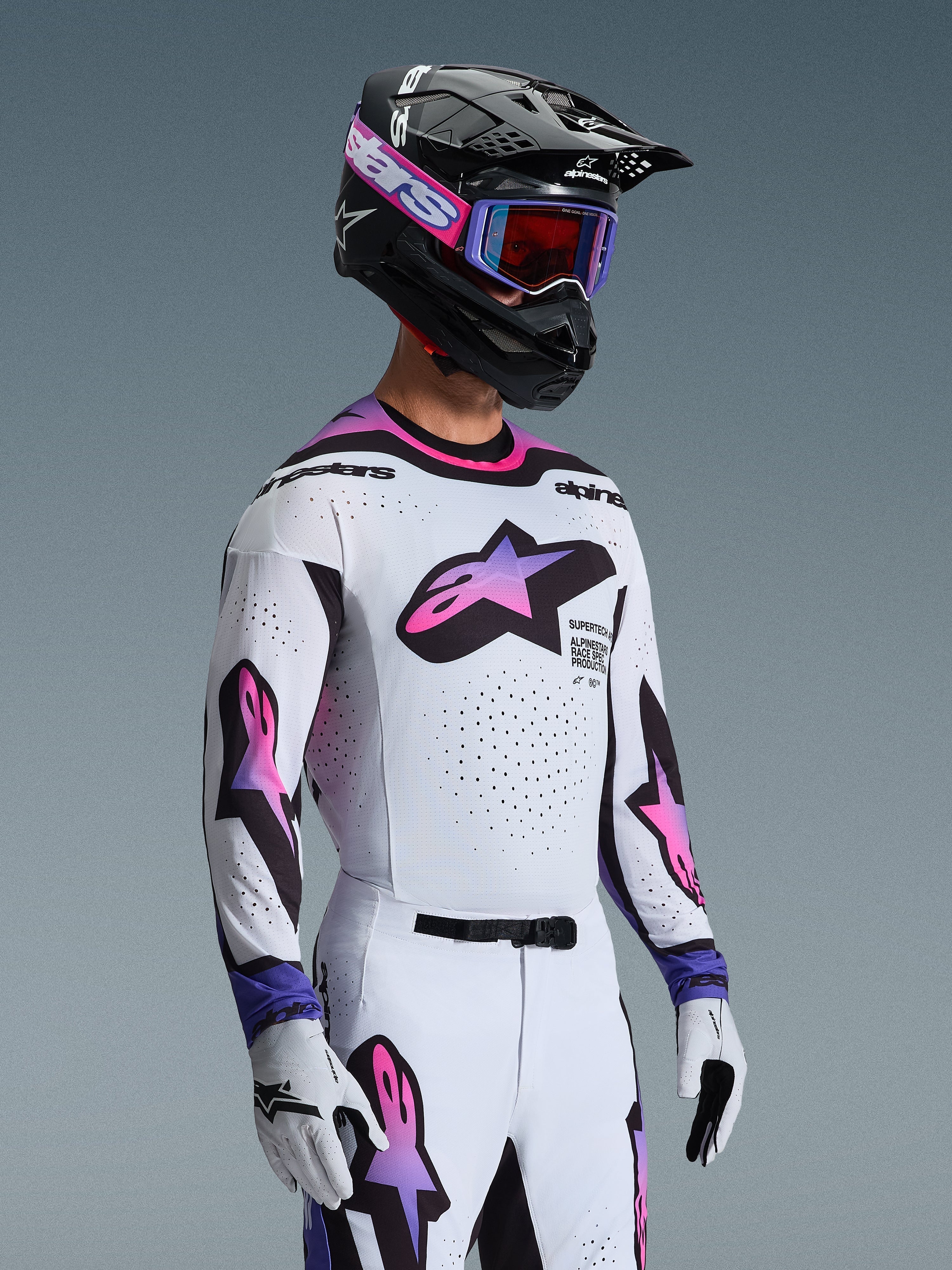 Pilota di motocross con maglia Supertech AFD Vista 2026 in bianco, viola e nero, pantaloni coordinati bianchi e viola, casco nero con occhiali viola e guanti bianchi, abbigliamento professionale completo da gara fuoristrada.