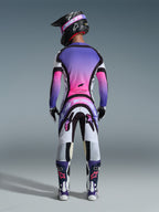 Pilota di motocross visto da dietro con maglia 2026 Supertech AFD Vista, bianco, viola e nero con sfumature rosa, pantaloni da motocross coordinati, casco nero con occhiali rosa e stivali bianchi e viola, set completo di abbigliamento professionale da gara