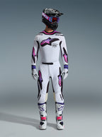 Pilota di motocross con completo Alpinestars 2026 Supertech AFD Vista, maglia e pantaloni bianchi con accenti viola, rosa e neri, casco nero con logo viola e occhiali blu, stivali bianchi con dettagli rosa, abbigliamento professionale coordinato per gare fuoristrada