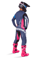 Pilota di motocross visto da dietro, completo Alpinestars 2025 Techstar Dreem, grigio con vivaci accenti rosa e bianchi, casco nero e bianco e stivali rosa acceso, abbigliamento completo da gara per motocross