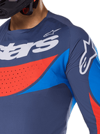 Primo piano della maglia Alpinestars Techstar Dreem 2025, blu navy con vivaci accenti blu e arancione, branding Alpinestars bianco su petto e spalla, con perforazioni tagliate al laser per la ventilazione