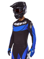 Pilota di motocross con il set Alpinestars Techstar Dreem 2025, maglia nera con pannelli blu stile traforato e branding bianco, pantaloni coordinati neri e blu, casco da corsa nero e guanti blu, abbigliamento tecnico per motocross off-road.