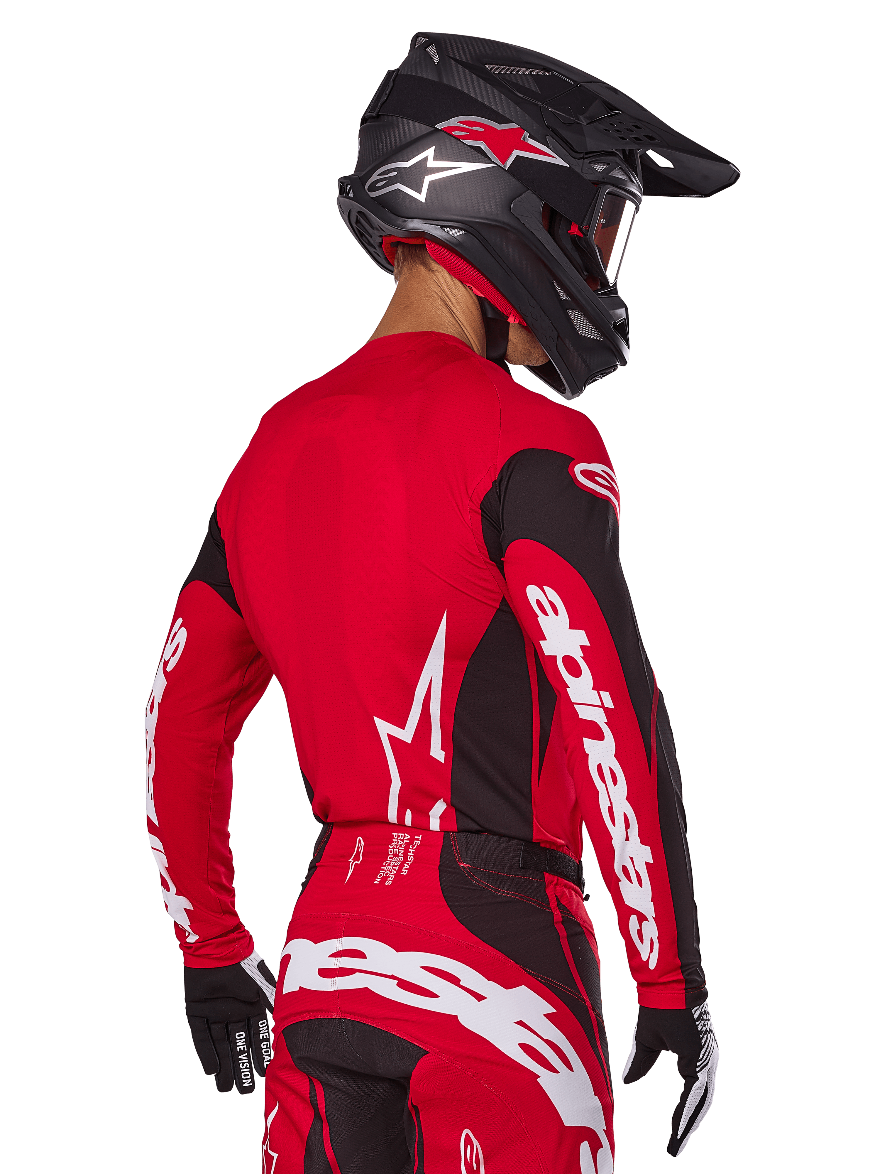 Pilota di motocross visto da dietro con completo Alpinestars Techstar Dreem 2025, maglia rossa e nera con loghi bianchi sulle maniche, pantaloni coordinati rossi e neri con logo bianco sulla seduta, casco in carbonio nero con accenti rossi, guanti bianchi e neri, abbigliamento professionale da gara fuoristrada