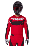 Alpinestars 2025 Techstar Dreem Jersey, maglia da motocross, rosso acceso e nero, con logo 'astars' bianco e pannello ventilato nero sul petto, indossata con pantaloni coordinati, casco nero e guanti bianchi e neri, per gare off-road professionali
