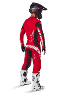 Pilota di motocross che indossa il set completo Alpinestars Techstar Dreem 2025 in rosso acceso e nero, con loghi bianchi su maglia e pantaloni, abbinato a casco nero, stivali bianchi e neri e guanti neri e bianchi, vista posteriore di tre quarti.