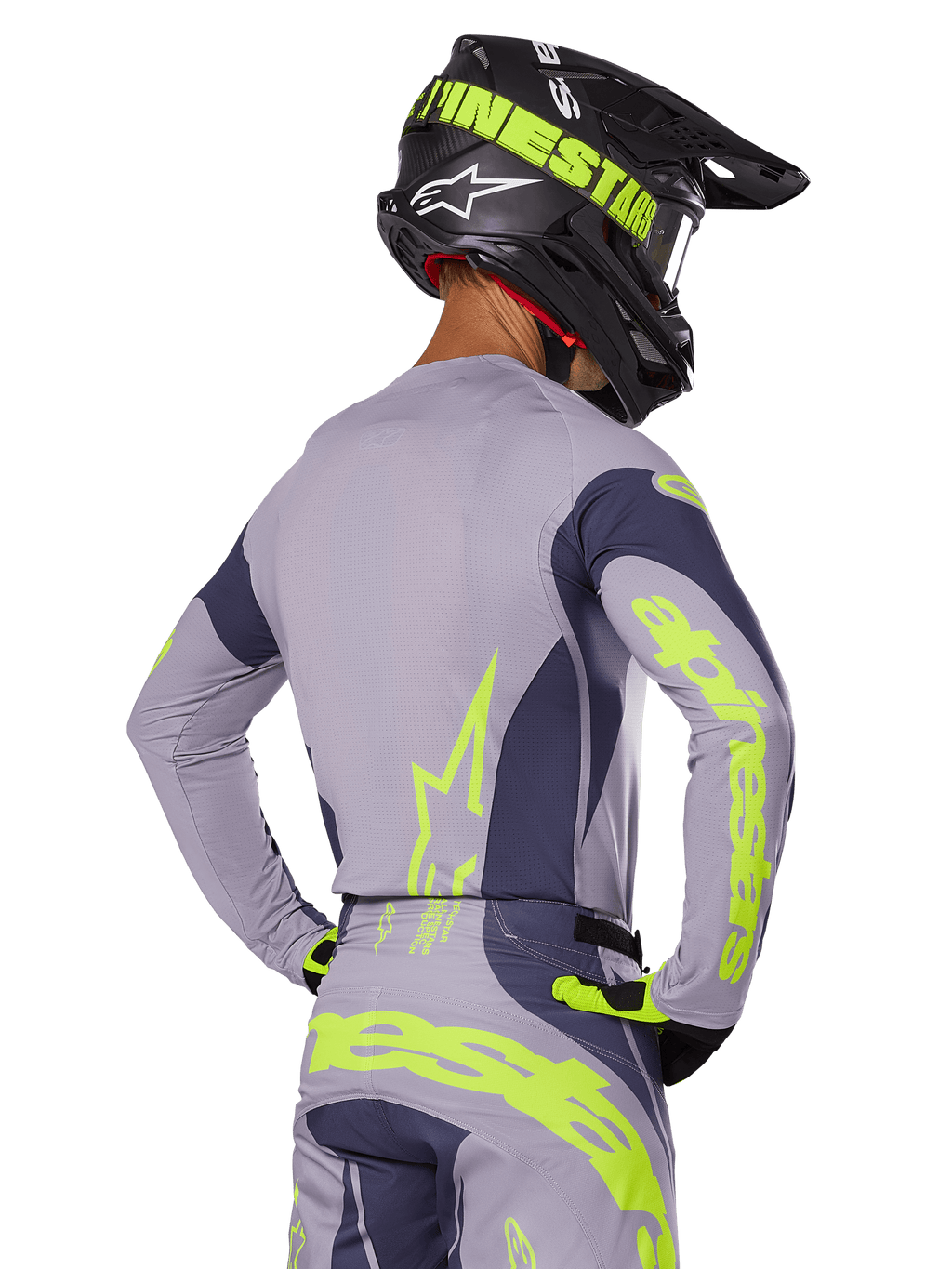 Pilota di motocross visto da dietro che indossa il set Alpinestars Techstar Dreem 2025, maglia e pantaloni grigi con vivace branding giallo-verde neon, casco nero coordinato con grafiche neon, completo professionale da motocross