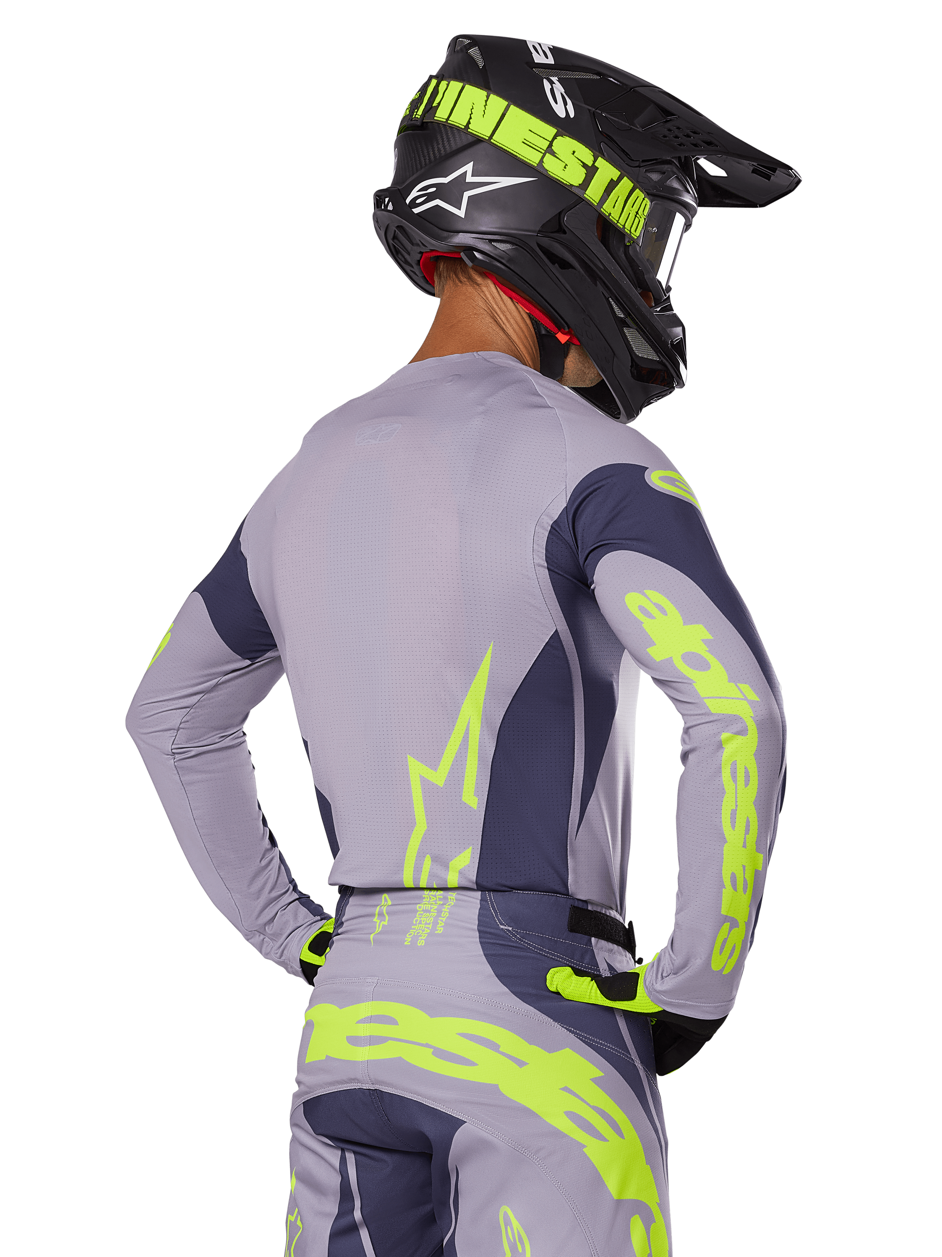 Pilota di motocross visto da dietro che indossa il set Alpinestars Techstar Dreem 2025, maglia e pantaloni grigi con vivace branding giallo-verde neon, casco nero coordinato con grafiche neon, completo professionale da motocross