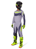 Set abbigliamento Alpinestars Techstar Dreem 2025, pilota di motocross in tenuta da gara completa, maglia e pantaloni grigi con motivi grigio scuro e dettagli giallo neon, casco nero coordinato, guanti e stivali giallo neon, equipaggiamento tecnico da fuoristrada