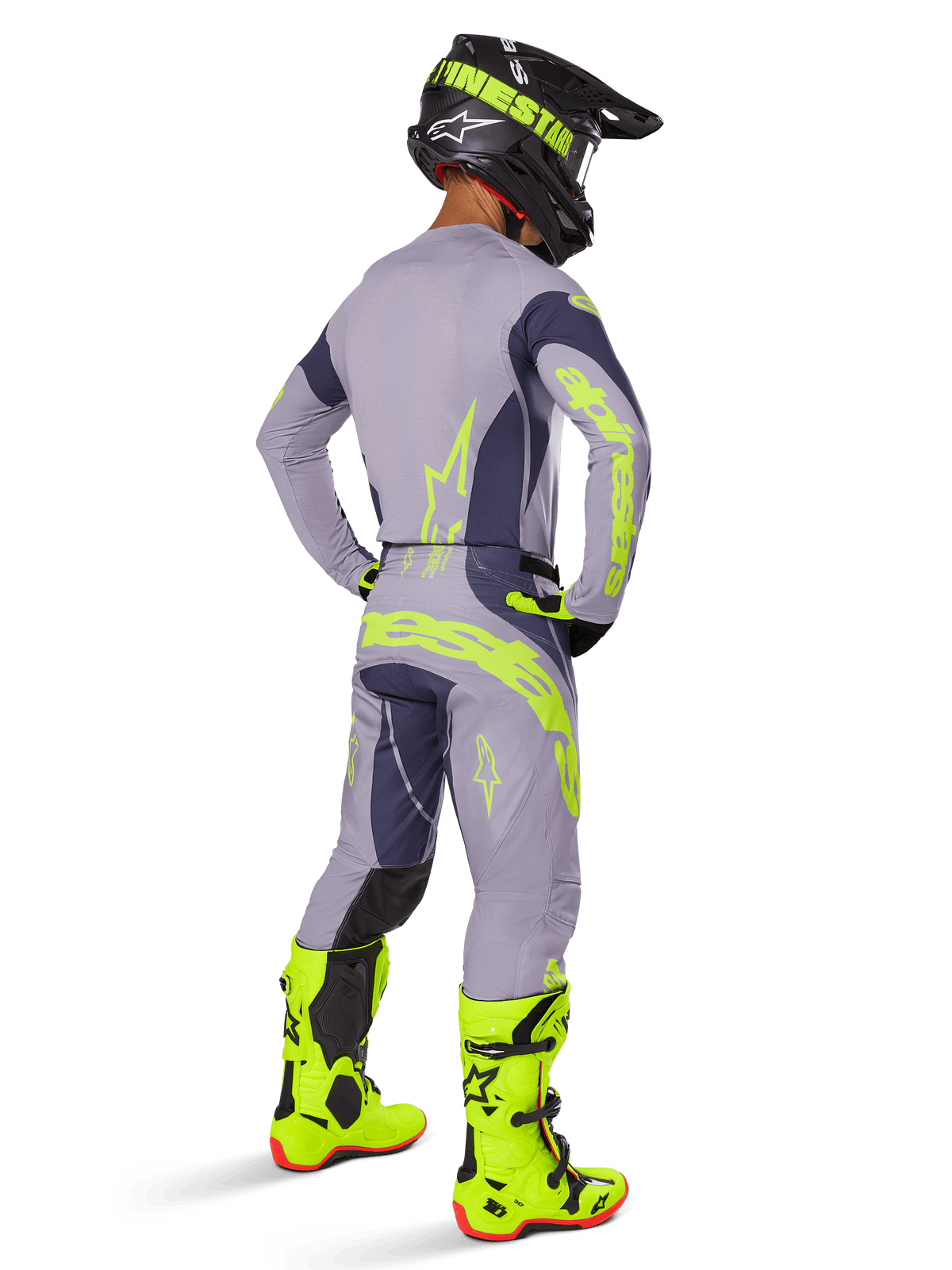 Pilota di motocross visto da dietro che indossa il set Alpinestars 2025 Techstar Dreem, grigio e grigio scuro con loghi giallo fluorescente, maglia e pantaloni coordinati, casco nero con accenti gialli e stivali giallo fluorescente, completo professionale da motocross.