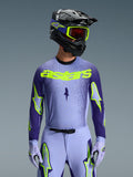 Maglia Alpinestars Supertech Scenz 2026, maglia da motocross, viola e giallo fluo, indossata da un pilota con casco coordinato nero e viola, occhiali giallo neon e pantaloni da corsa viola, con marchio astars giallo neon sul petto e loghi a stella sulle maniche.