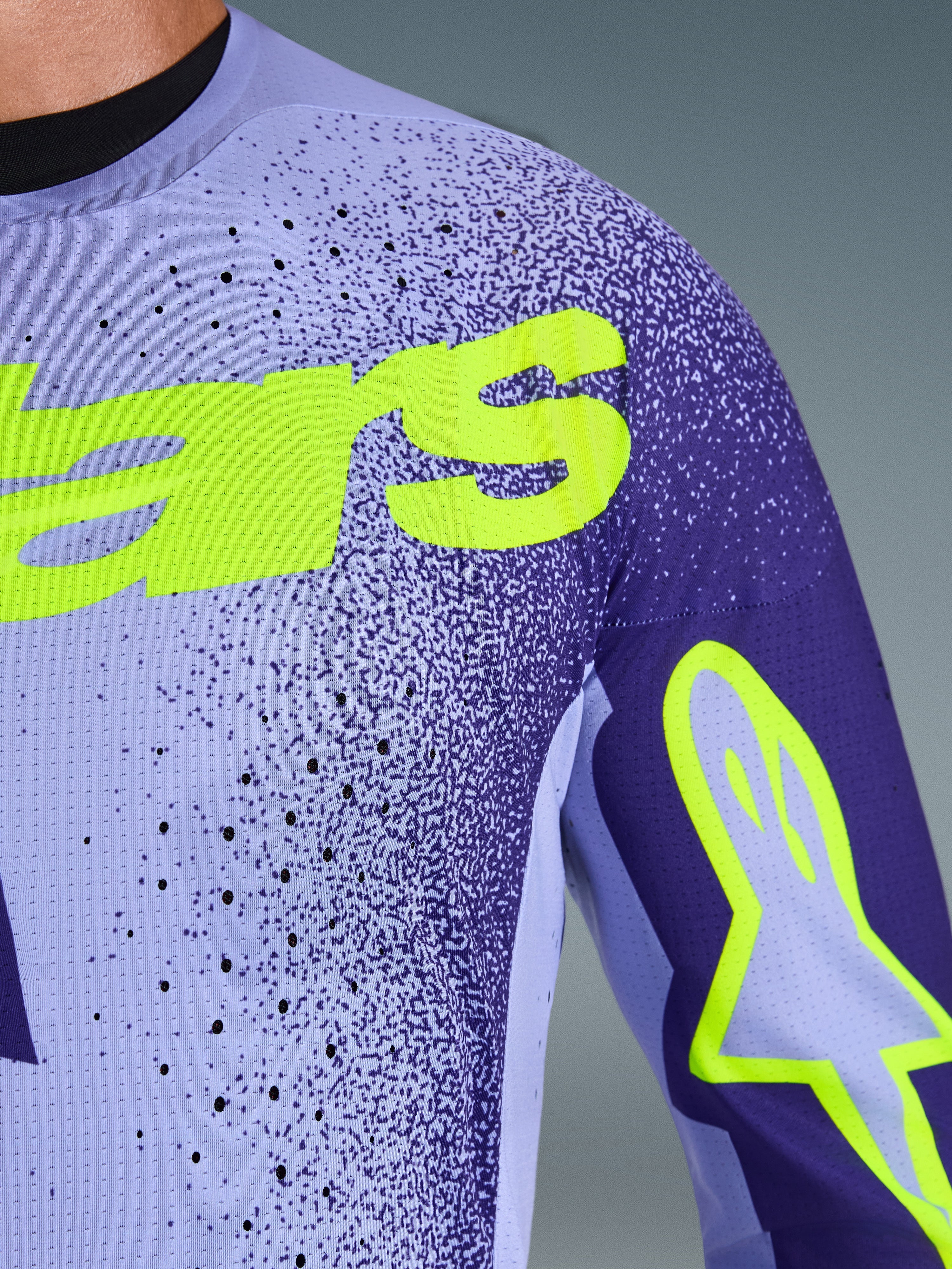 Maglia Alpinestars Supertech Scenz 2026 in Viola Giallo Fluo, primo piano di petto e spalla con perforazioni laser, materiale mesh elasticizzato e branding giallo fluo per prestazioni motocross professionali.