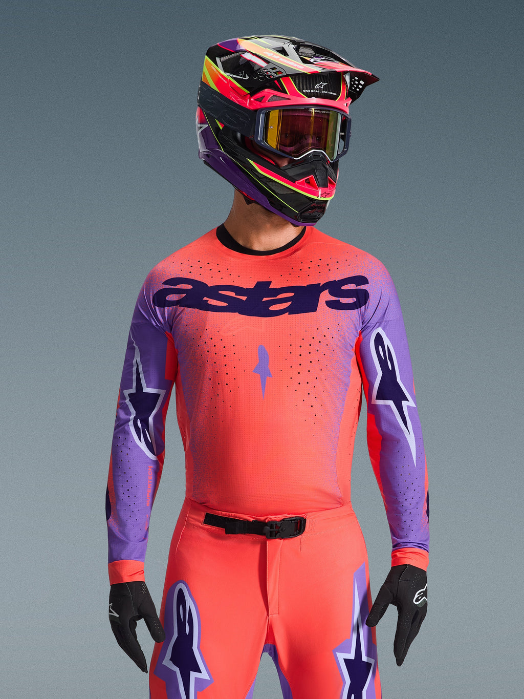 Alpinestars 2026 Supertech Scenz Jersey, maglia da motocross, arancione corallo e viola, con grande scritta 'astars' e design a stelle sulle maniche, indossata con pantaloni coordinati e casco multicolore, abbigliamento racing per fuoristrada