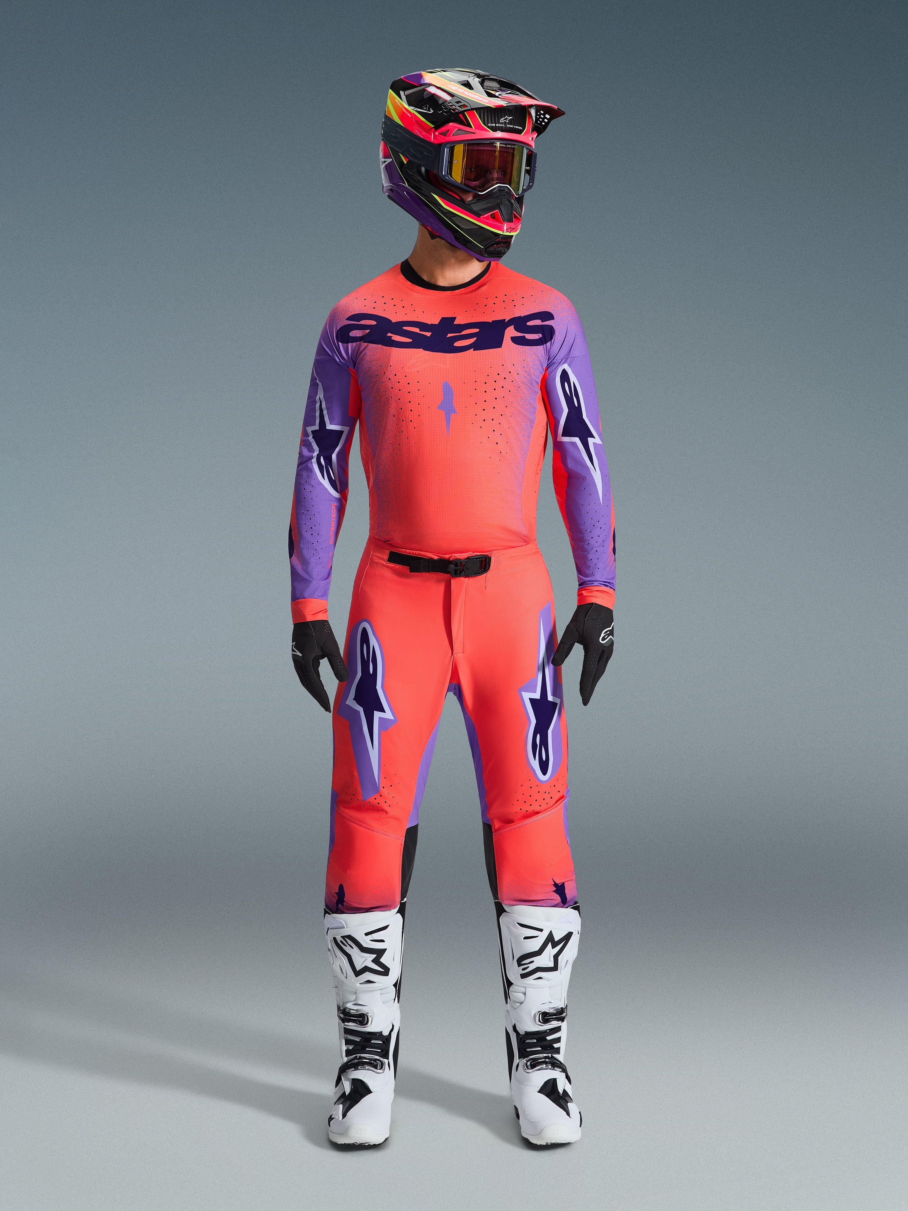 Set Abbigliamento Supertech Scenz 2026, completo da motocross Alpinestars, rosso-arancio vibrante e viola, maglia con marchio 'astars' nero, pantaloni coordinati con loghi a stella viola, casco da corsa colorato e stivali bianchi, kit professionale per prestazioni fuoristrada