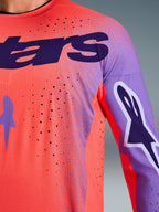 Alpinestars 2026 Supertech Scenz Jersey, maglia da motocross, corallo acceso e viola, vista ravvicinata con trama in mesh traspirante e perforazioni laser, grande logo viola sul petto e grafiche sulle maniche, per gare fuoristrada professionali.