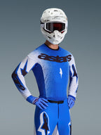 Maglia Alpinestars Supertech Scenz 2026, maglia da motocross, blu UCLA e bianco, indossata come set completo con pantaloni e guanti blu coordinati, logo 'astars' nero, casco bianco e occhiali scuri, vestibilità racing professionale.