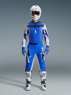 Pilota di motocross che indossa il set completo Alpinestars 2026 Supertech Scenz in Ucla Blue e bianco, con maglia leggera blu e bianca con loghi neri, pantaloni blu coordinati, casco da gara bianco e stivali da motocross bianchi, abbigliamento di livello professionale per gare off-road.