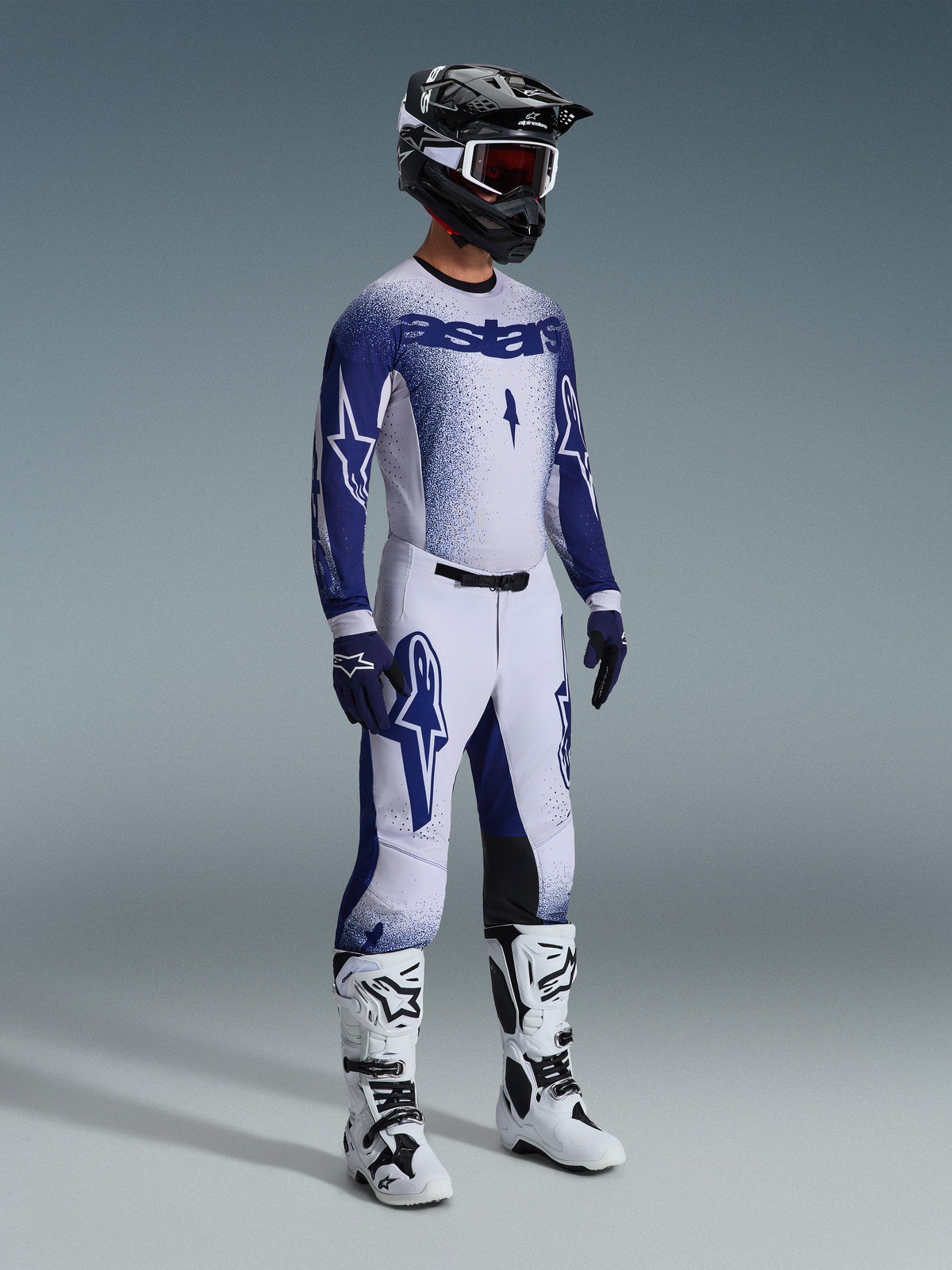 Set completo Alpinestars Supertech Scenz 2026, pilota di motocross con maglia e pantaloni bianchi e blu navy, effetto sfumato puntinato, logo Astars, casco bianco e nero, guanti blu navy e stivali da motocross bianchi