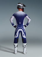 Pilota di motocross visto di spalle che indossa la maglia Alpinestars 2026 Supertech Scenz, grigio chiaro e blu scuro con design sfumato punteggiato, pantaloni da motocross coordinati, stivali da corsa bianchi e casco nero, completo da gara fuoristrada.