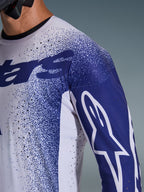 Primo piano della Maglia Alpinestars Supertech Scenz 2026 in grigio chiaro e blu scuro, con perforazioni tagliate al laser, motivo grafico puntinato, logo Astars bianco sulla manica, vestibilità tecnica da motocross professionale