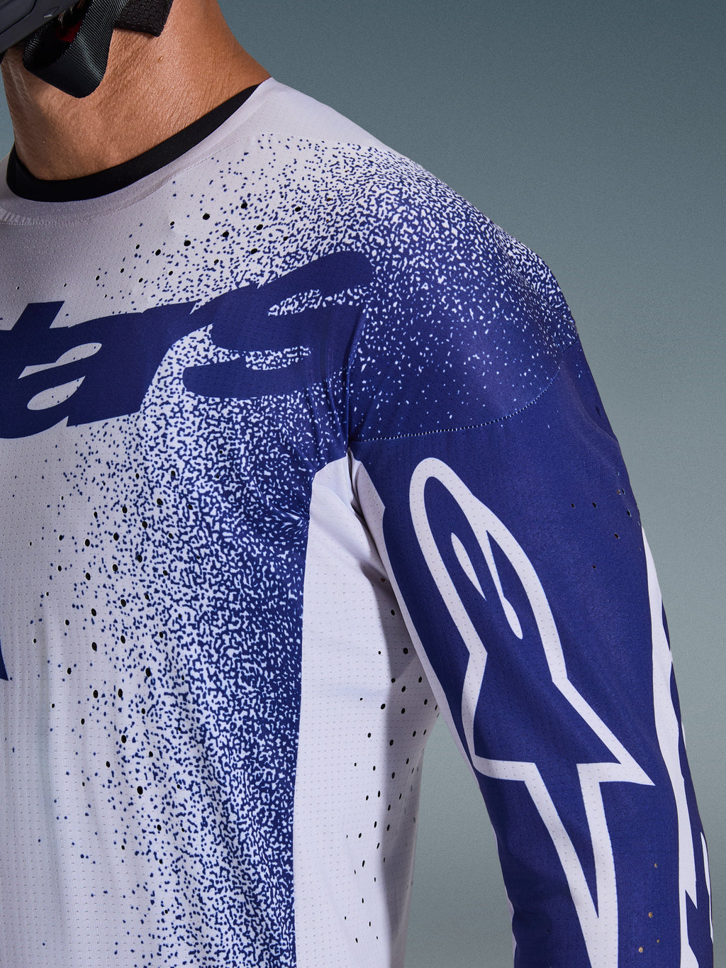 Maglia Alpinestars Supertech Scenz 2026, grigio chiaro e blu scuro, primo piano di spalla e petto con perforazioni tagliate al laser, logo Astars bianco sulla manica blu, grafica puntinata, abbigliamento professionale da motocross.