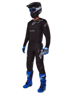 Set completo motocross Alpinestars Racer Graphite 2025, outfit completo da motocross, maglia e pantaloni neri e grigi con loghi argento, casco nero con occhiali a lenti blu, guanti blu e neri, stivali blu brillante, equipaggiamento professionale per gare fuoristrada
