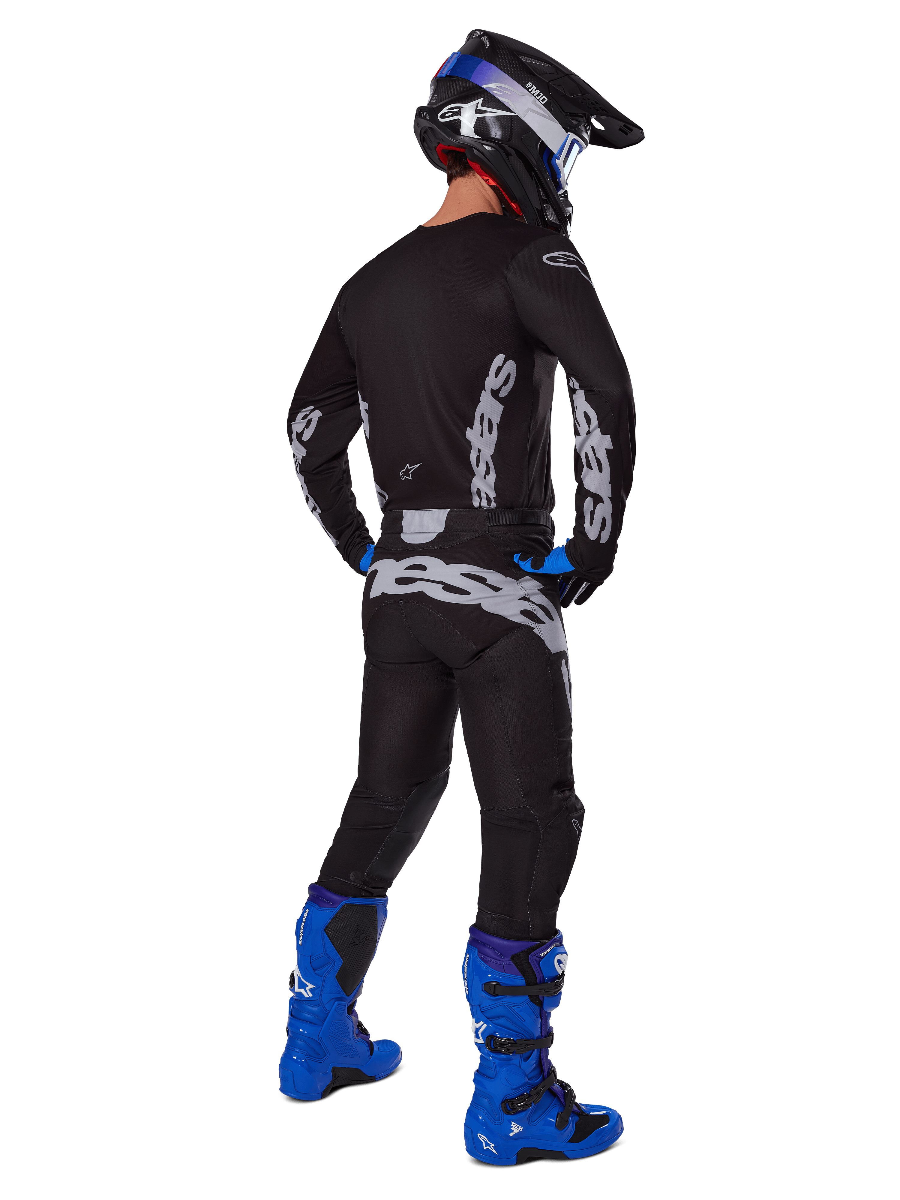 Pilota di motocross visto da dietro che indossa il set Alpinestars 2025 Racer Graphite, maglia e pantaloni nero e grigio con branding grigio, abbinati a stivali da motocross blu acceso, casco nero e blu e guanti blu, abbigliamento completo da fuoristrada ad alte prestazioni.