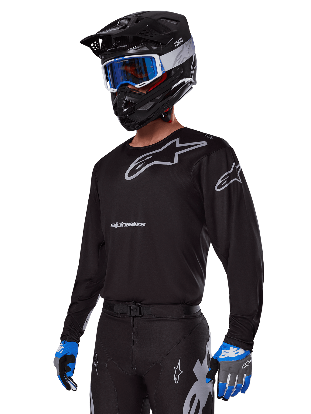 Pilota di motocross con Set Gear Alpinestars Racer Graphite 2025, maglia nera con loghi Alpinestars grigi, pantaloni neri coordinati con dettagli grigi, casco nero con occhiali blu e bianchi, guanti blu e grigi, abbigliamento tecnico per corse fuoristrada