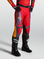 Alpinestars Pantaloni Racer Hunt, pantaloni motocross da uomo, rosso e grigio con dettagli corallo, indossati da un modello con stivali neri, certificati per prestazioni off-road.