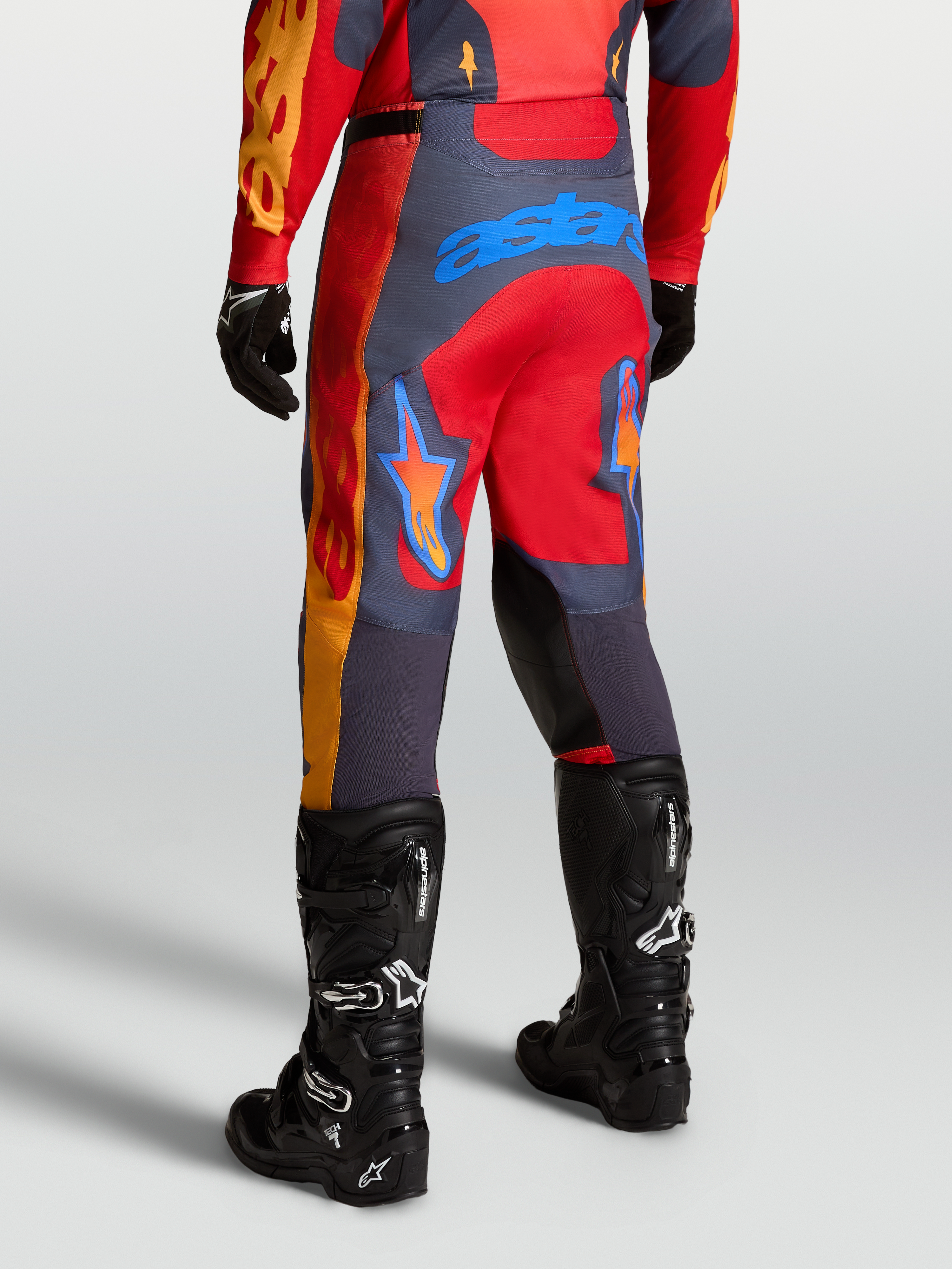 Alpinestars Pantaloni Racer Hunt, pantaloni da motocross racing in rosso fire e grigio stone, vista posteriore con stivali tecnici neri.