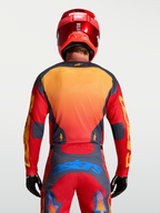 Alpinestars Maglia Racer Hunt, maglia motocross da uomo, rosso fuoco e grigio con dettagli gialli e blu, vista posteriore su modello con casco e guanti