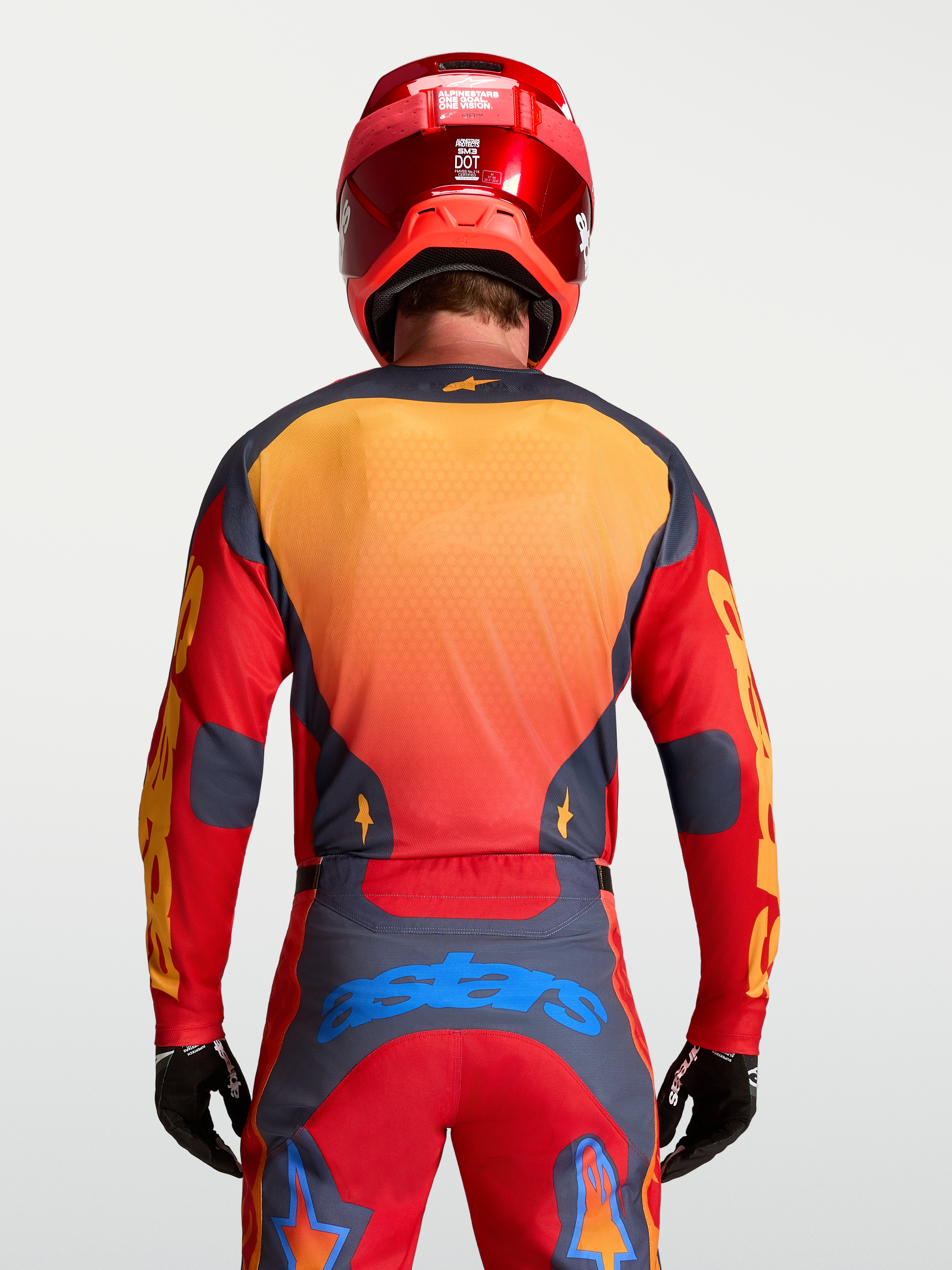 Alpinestars Maglia Racer Hunt, maglia motocross da uomo, rosso fuoco e grigio con dettagli gialli e blu, vista posteriore su modello con casco e guanti