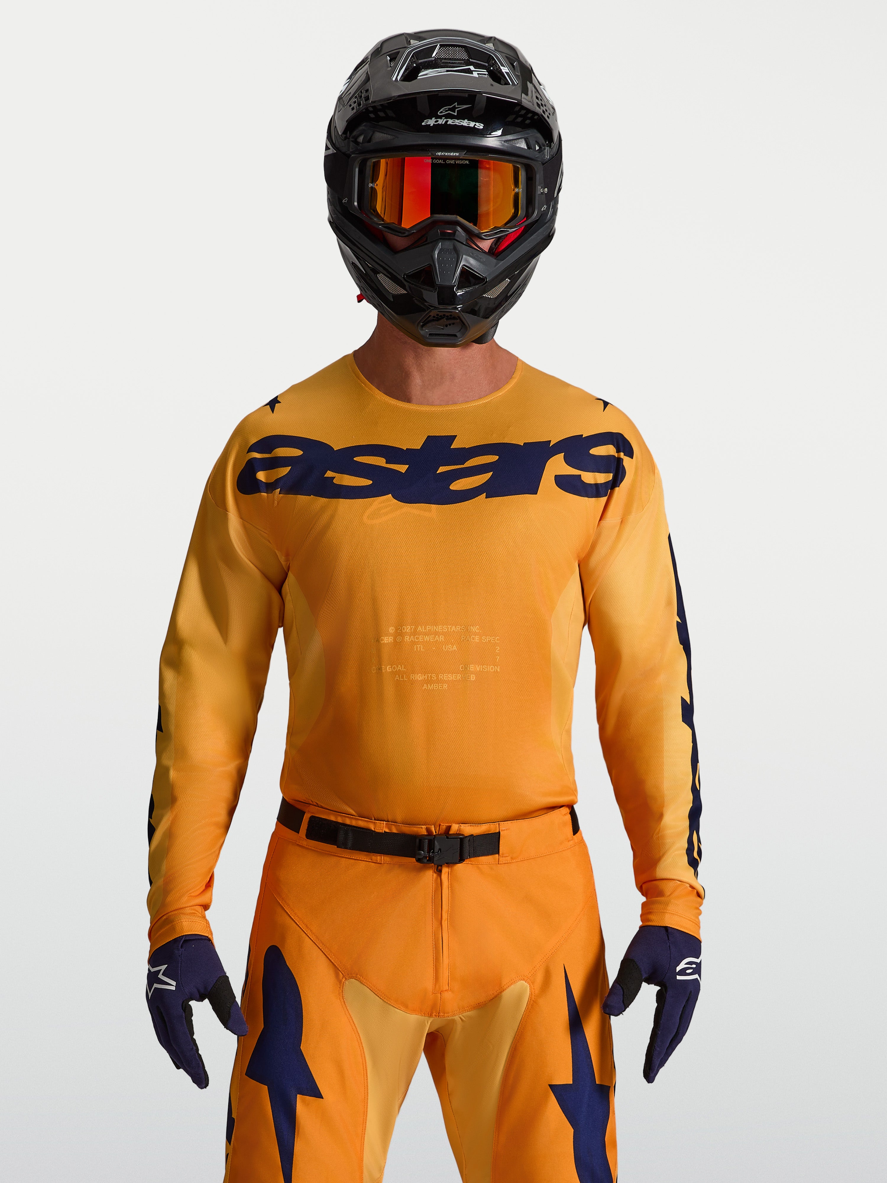 Alpinestars Maglia Racer Amber, maglia da motocross per uomo, arancione e blu scuro, in poli-tessuto traspirante, indossata con abbigliamento racing coordinato.