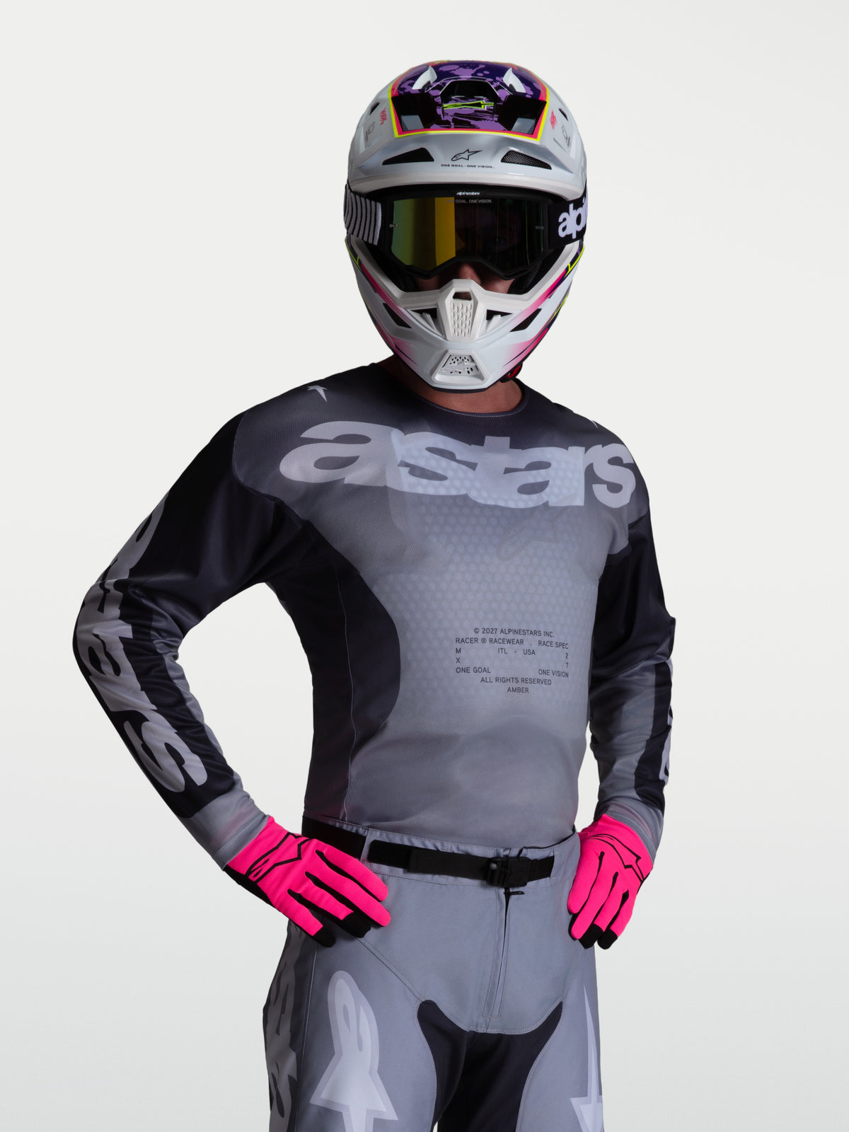 Alpinestars Maglia Racer Amber, maglia da motocross per uomo, grigio e lilla, indossata da un pilota con casco e guanti, pannelli in mesh traspirante per prestazioni off-road.