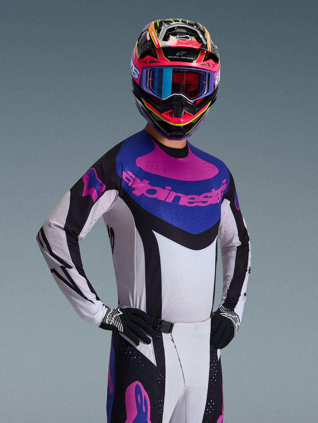 Alpinestars Techstar Knif Jersey 2026, maglia da motocross, nero, grigio chiaro e viola, indossata da un pilota con equipaggiamento completo, telaio bianco con accenti neri e pannello blu sul petto con logo Alpinestars viola, vestibilità racing per il fuoristrada