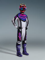 Pilota di motocross che indossa la maglia Alpinestars 2026 Techstar Knif in Nero Grigio Chiaro Viola, pantaloni coordinati con grandi loghi rosa, stivali viola e un casco multicolore con occhiali blu, kit da gara completo per prestazioni off-road