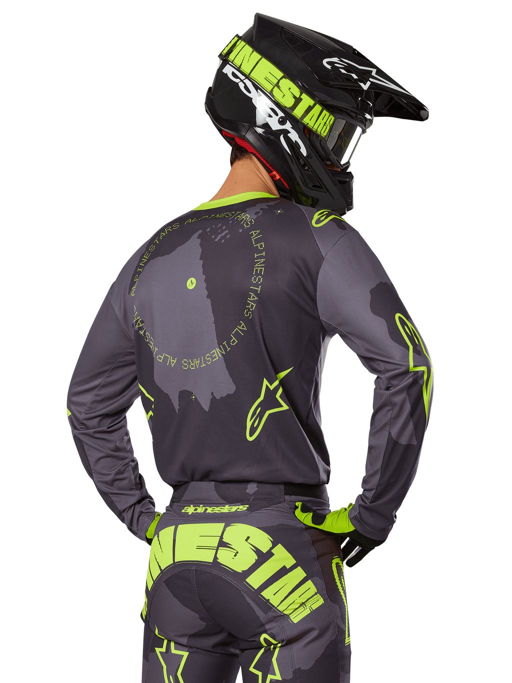 Pilota di motocross visto da dietro, completo Alpinestars 2025 Racer Hollow, maglia grigia con scritte circolari e loghi a stella giallo fluorescente, pantaloni grigi e gialli con branding evidente sulla seduta, casco nero e verde lime, abbigliamento per corse fuoristrada