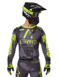 Alpinestars 2025 Racer Hollow Jersey, maglia da motocross, mimetico scuro e giallo neon, indossata con pantaloni coordinati, casco nero e giallo con occhiali e guanti neri, con logo Alpinestars e design mimetico