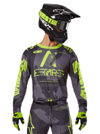 Alpinestars 2025 Racer Hollow Jersey, maglia da motocross, mimetico scuro e giallo neon, indossata con pantaloni coordinati, casco nero e giallo con occhiali e guanti neri, con logo Alpinestars e design mimetico