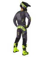 Pilota di motocross visto di spalle che indossa la maglia e i pantaloni Alpinestars 2025 Racer Hollow in Dark Camo Yellow Fluo, con motivo mimetico grigio scuro e accenti giallo neon, abbinati a un casco nero e giallo e stivali giallo neon brillanti.