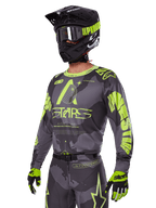Set Gear Alpinestars Racer Hollow 2025, maglia e pantaloni da motocross in grigio e giallo neon, indossati con casco, occhiali e guanti neri coordinati, caratterizzati da vistosi loghi Alpinestars giallo fluo e grafiche a stella su base grigia a fantasia, look professionale per corse fuoristrada.