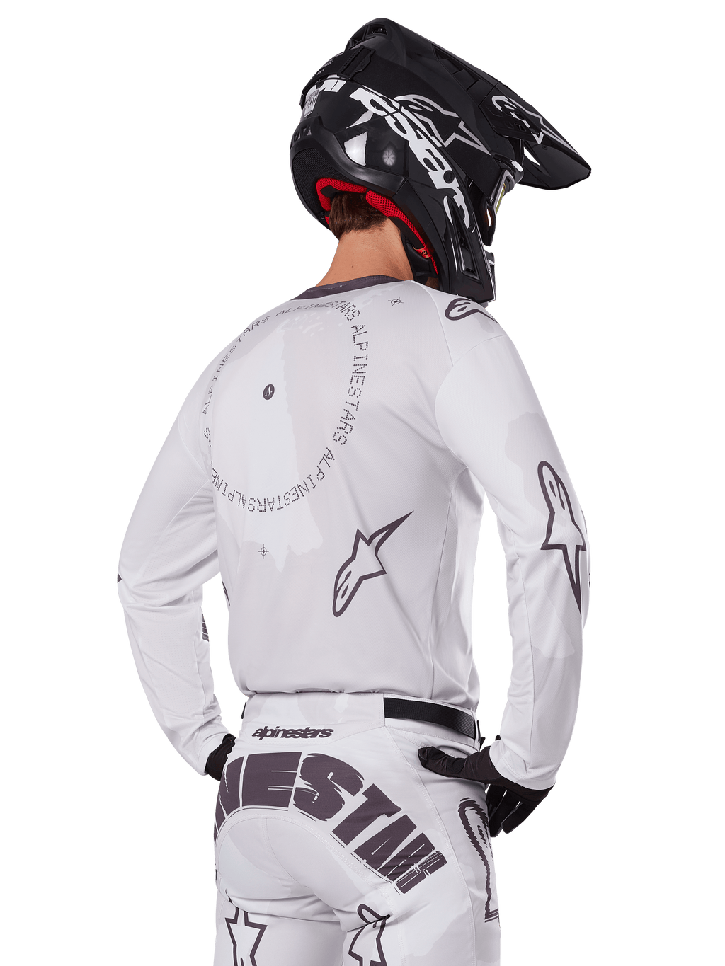 Pilota di motocross visto di spalle con il set completo Alpinestars 2025 Racer Hollow in bianco, maglia bianca a maniche lunghe con loghi a stella grigi e grafiche circolari, pantaloni bianchi coordinati con logo evidente sulla seduta, casco nero, abbigliamento da gara fuoristrada coordinato