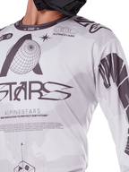 Primo piano della maglia Alpinestars Racer Hollow 2025, bianco e grigio, con stampe grafiche nere, logo del globo e codice binario, abbigliamento tecnico da motocross per la guida fuoristrada