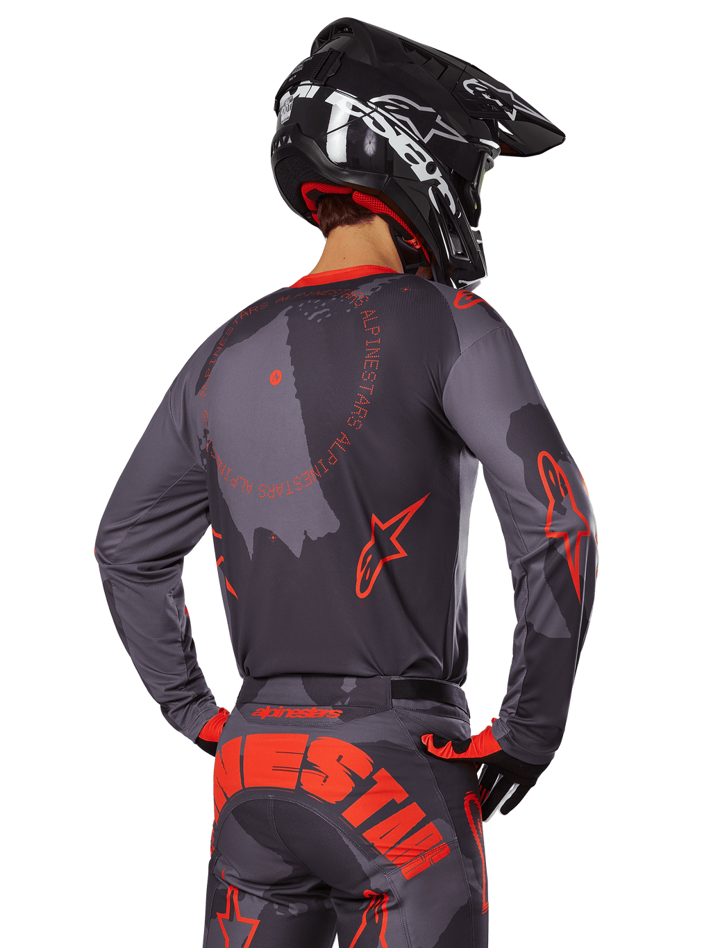 Maglia Alpinestars Racer Hollow 2025, vista posteriore di un pilota di motocross in completo Grigio Camo e Arancione Fluo, pantaloni coordinati con grande scritta Alpinestars arancione e casco nero, design professionale per fuoristrada