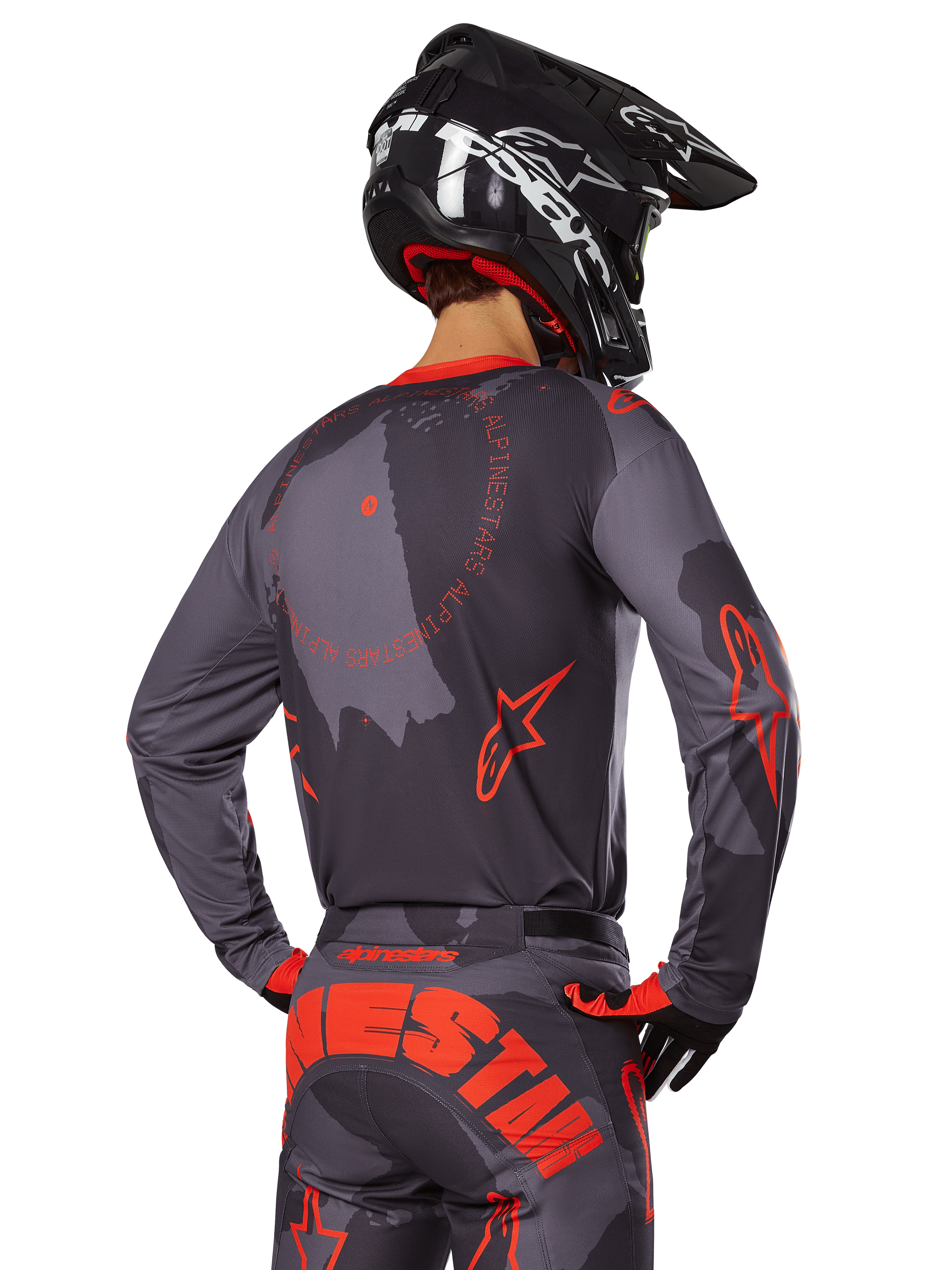 Maglia Alpinestars Racer Hollow 2025, vista posteriore di un pilota di motocross in completo Grigio Camo e Arancione Fluo, pantaloni coordinati con grande scritta Alpinestars arancione e casco nero, design professionale per fuoristrada