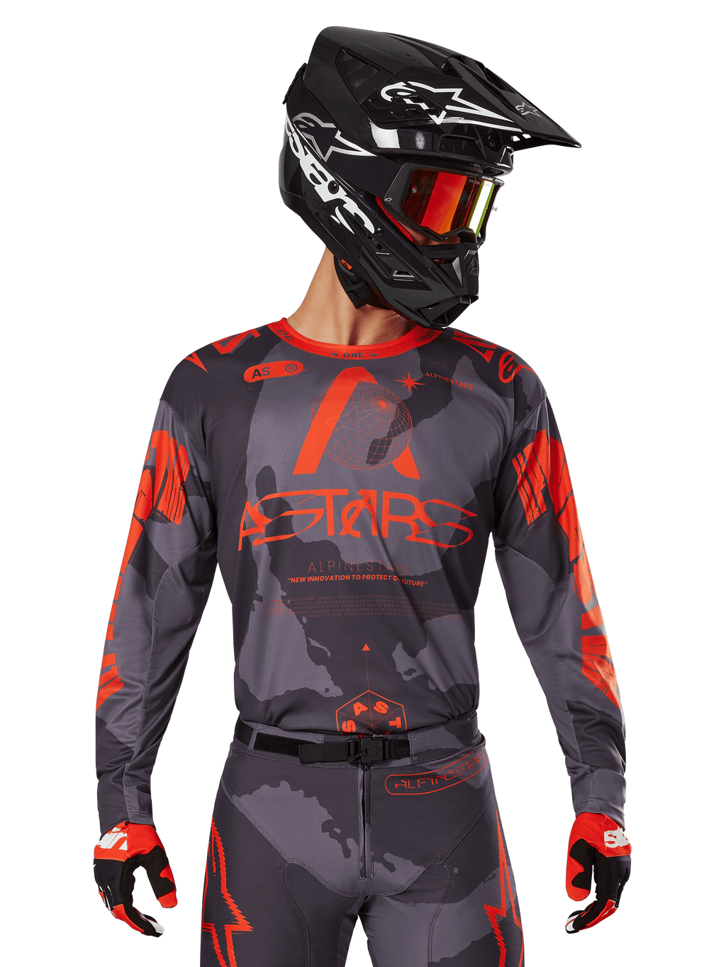 Alpinestars Maglia Racer Hollow 2025, maglia motocross grigio camo e arancione fluo, indossata con set coordinato di pantaloni e guanti, con casco nero con grafiche bianche e occhiali, branding ASTARS ben visibile, abbigliamento sportivo protettivo per corse fuoristrada