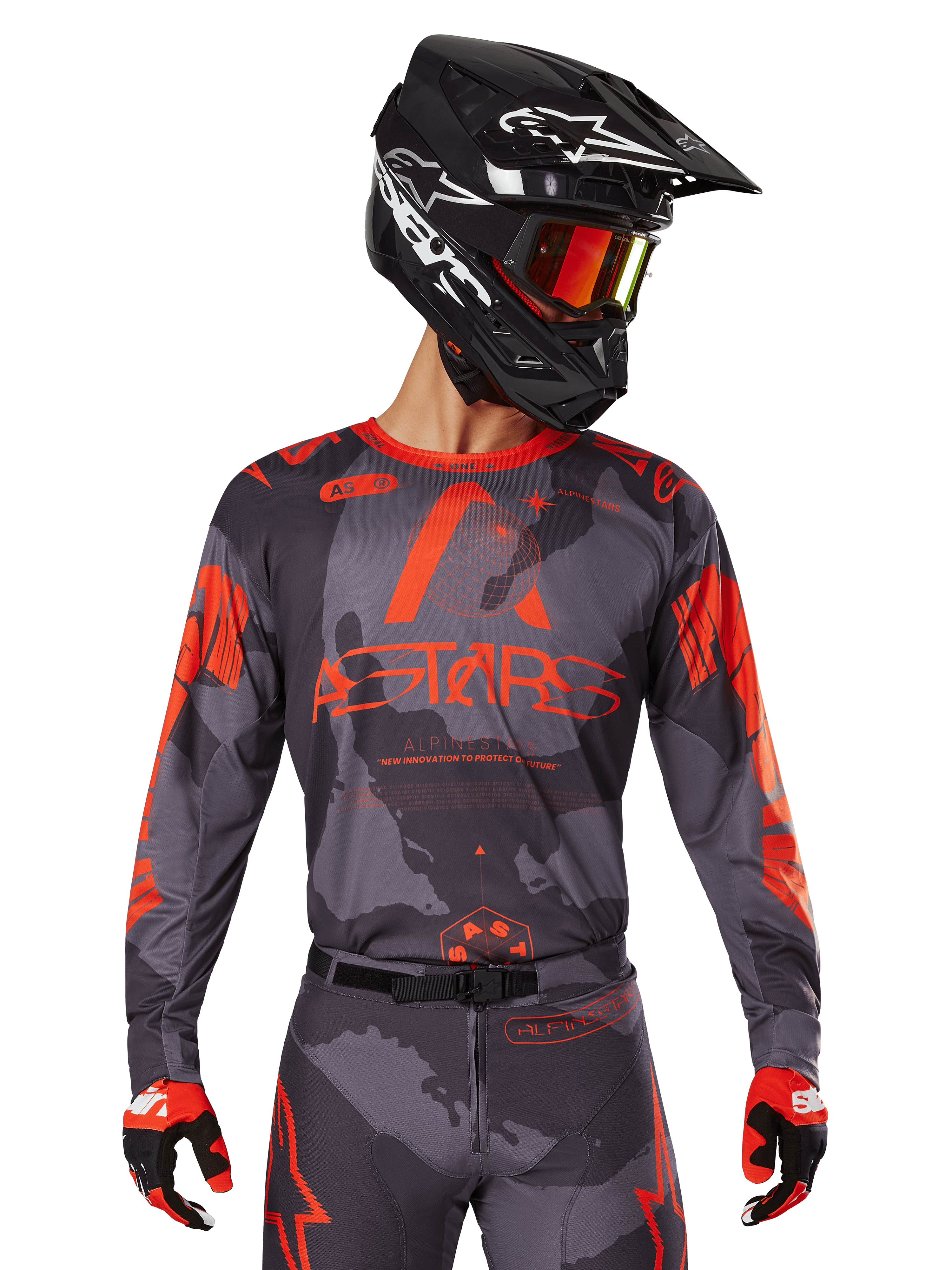 Alpinestars Maglia Racer Hollow 2025, maglia motocross grigio camo e arancione fluo, indossata con set coordinato di pantaloni e guanti, con casco nero con grafiche bianche e occhiali, branding ASTARS ben visibile, abbigliamento sportivo protettivo per corse fuoristrada