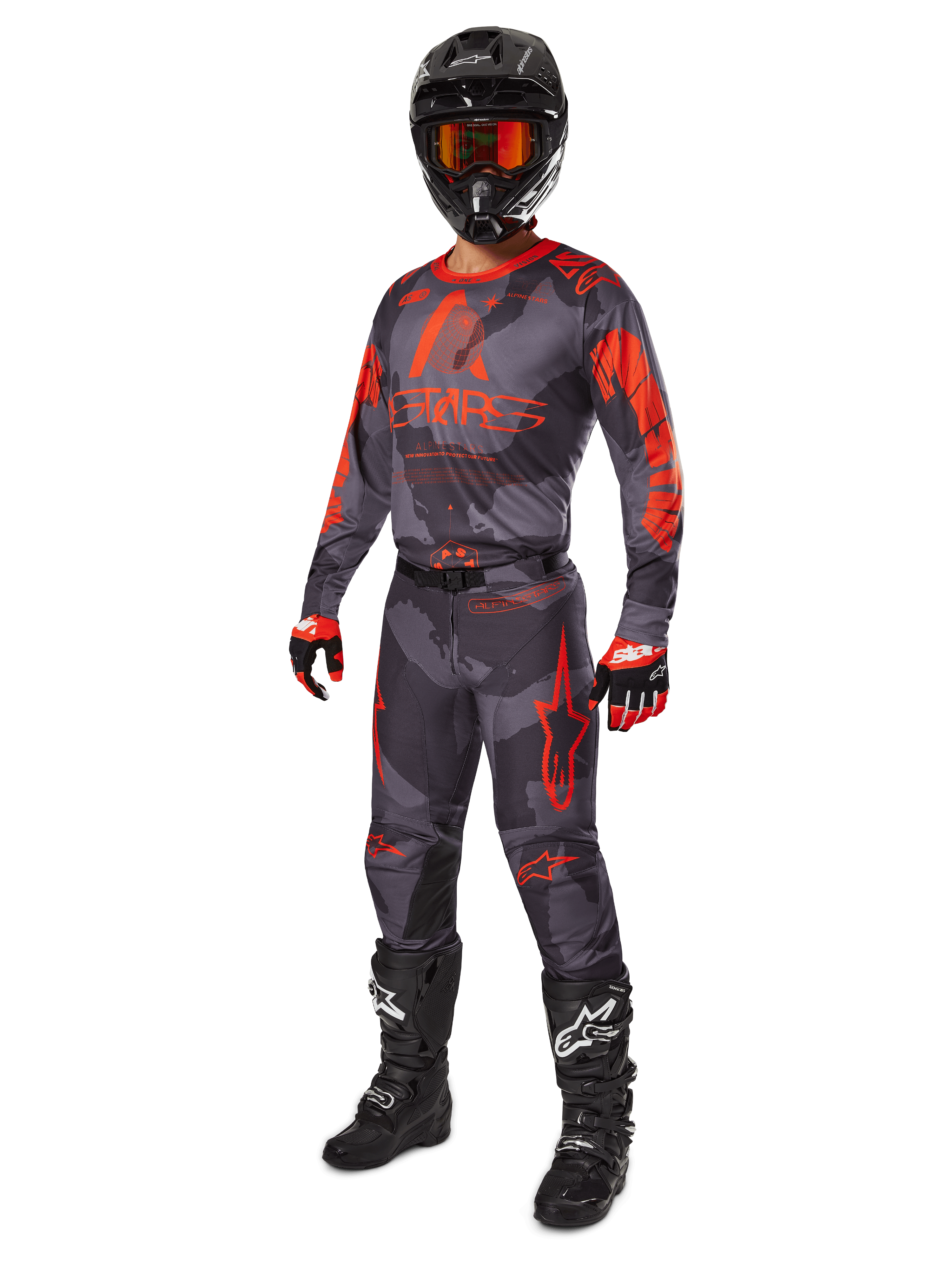 Pilota di motocross con abbigliamento da gara completo, maglia e pantaloni Alpinestars Racer Hollow 2025 in grigio camo arancione fluo, casco nero con occhiali arancioni, guanti neri e rossi e stivali neri con loghi bianchi, outfit coordinato per prestazioni fuoristrada