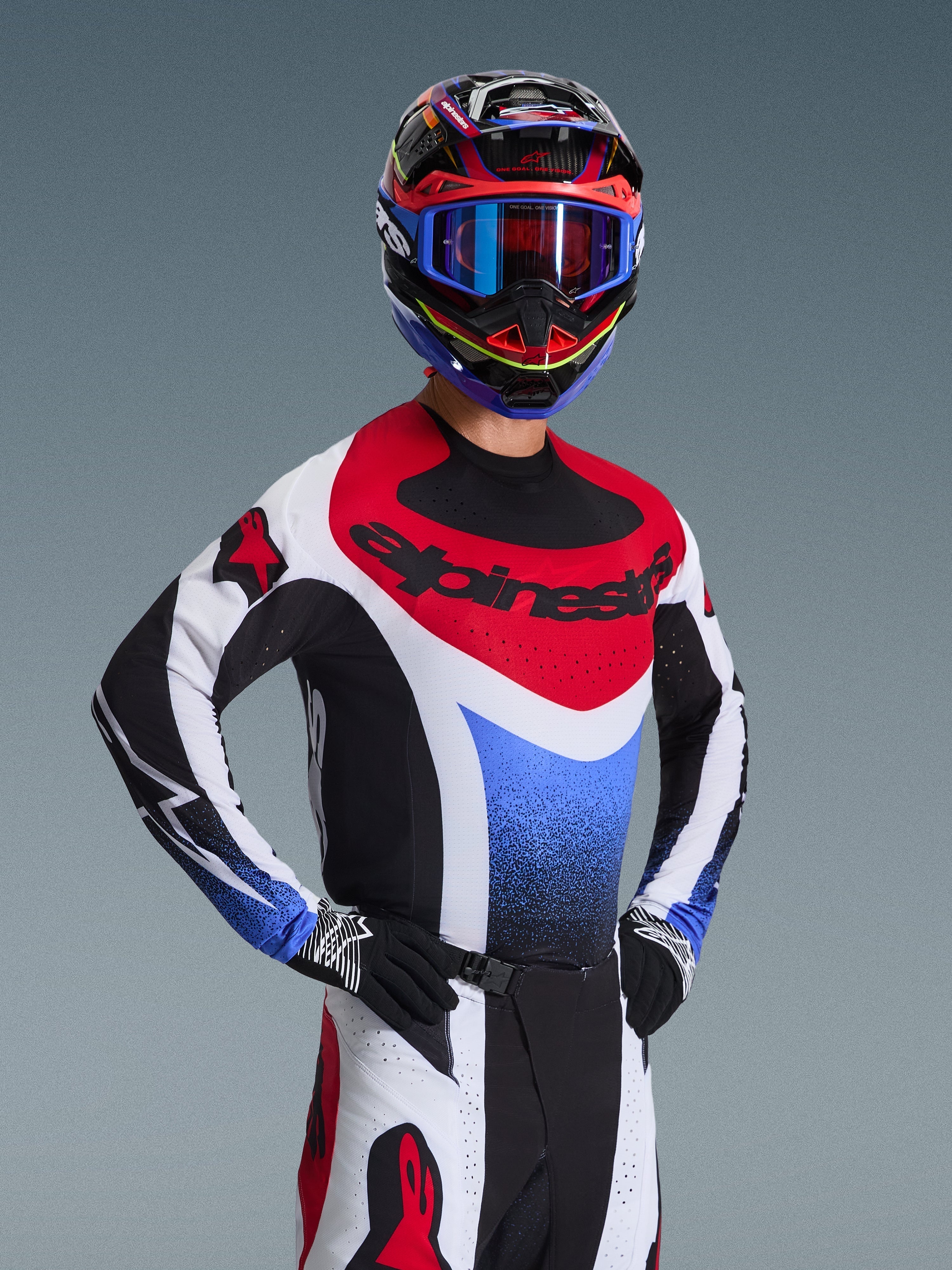 Pilota di motocross che indossa la maglia Alpinestars Techstar Knif 2026 in rosso, bianco e blu, con marchio nero sul petto, abbinata a pantaloni da motocross coordinati, casco da corsa con occhiali blu e guanti neri e bianchi, attrezzatura professionale da fuoristrada per competizioni